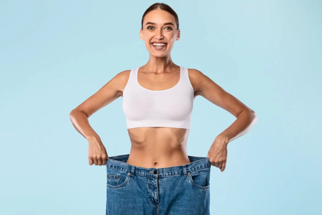 smiling woman holding oversized jeans weight loss utc